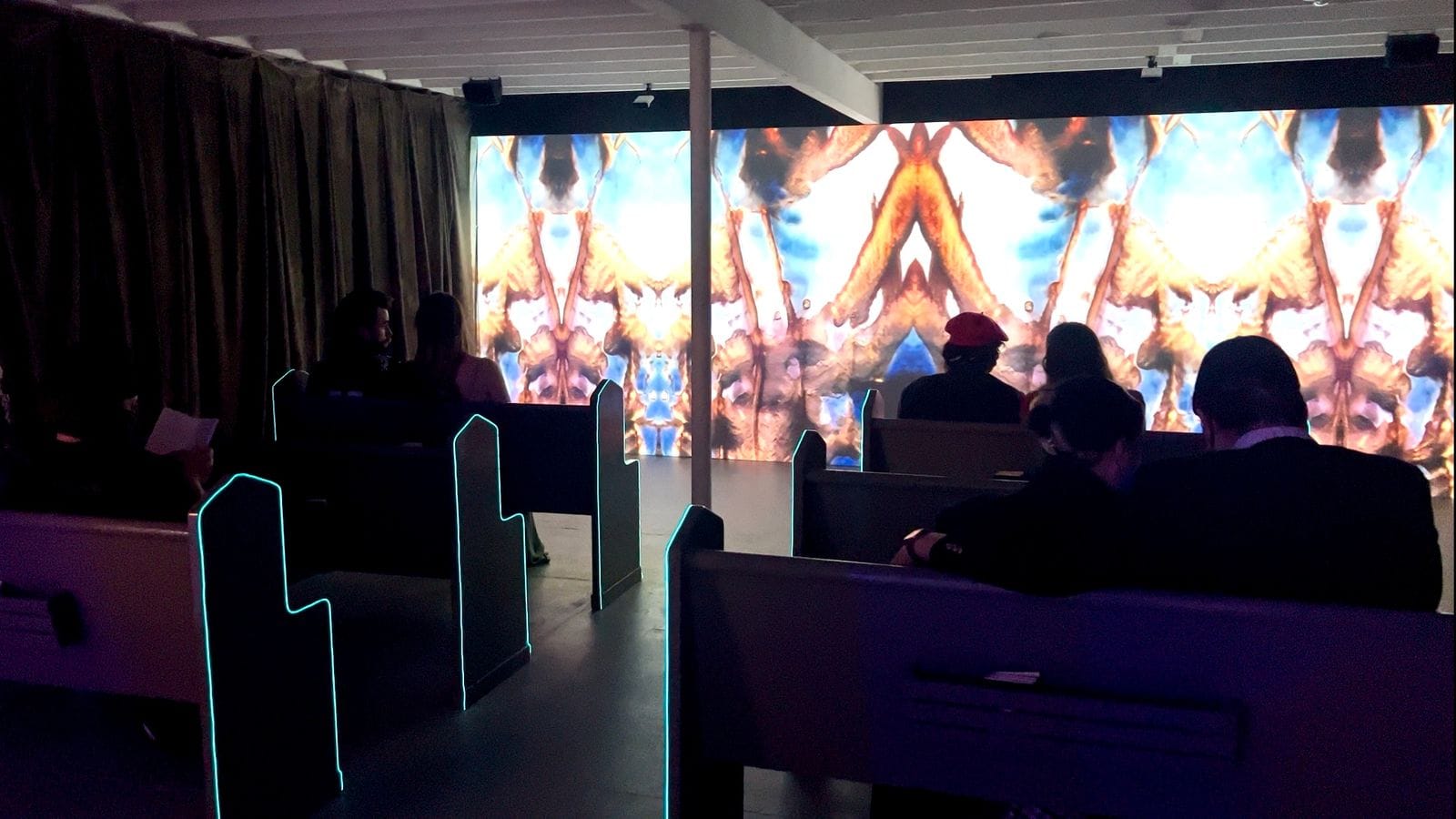 The Word of the Future — visitors seated in glowing pews before a large AI-generated stained-glass projection